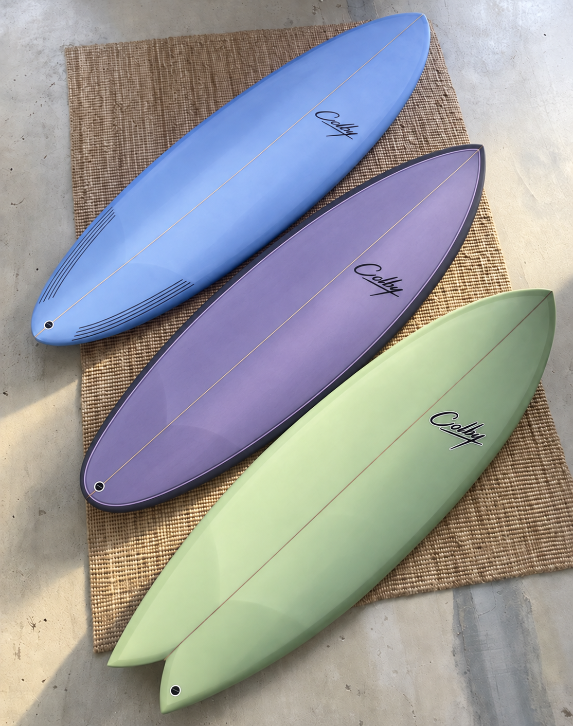 Blue Krypto Twin, lavender Crypto and pale green Modern Fish Colby surfboards arranged on a woven mat